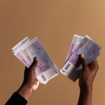 Close-up image of hands holding 500 euro banknotes on a neutral beige background.