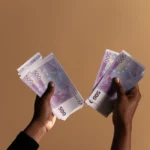 Close-up image of hands holding 500 euro banknotes on a neutral beige background.