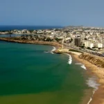 aerial view of a busy beach along a coastal city with buildings and railway tracks