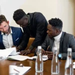 Three professionals working together at a table, discussing documents in an office setting.