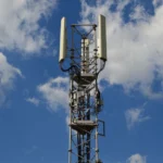 A tall cellular communication tower against a vivid blue sky, symbolizing modern technology.