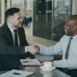 Two businessmen shaking hands across a table.
